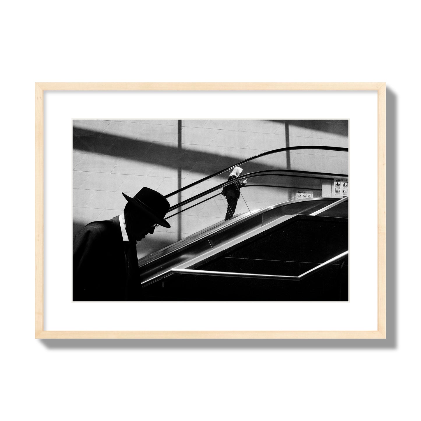 Fine art black and white street photograph of a man ascending an escalator. Archival pigment print, large size, natural wood frame.