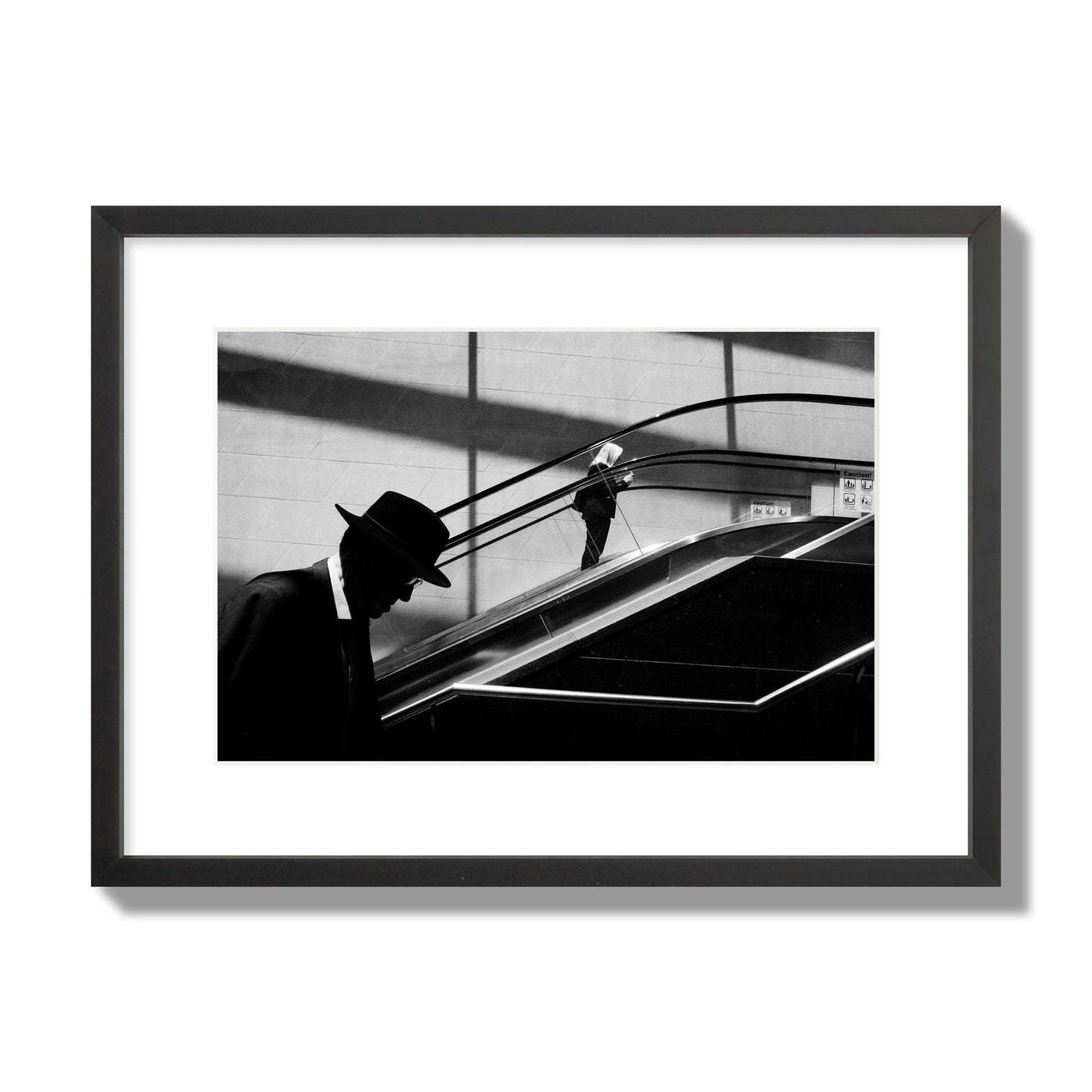Fine art black and white street photograph of a man ascending an escalator. Archival pigment print, medium size, black frame.