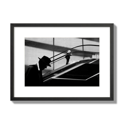 Fine art black and white street photograph of a man ascending an escalator. Archival pigment print, medium size, black frame.