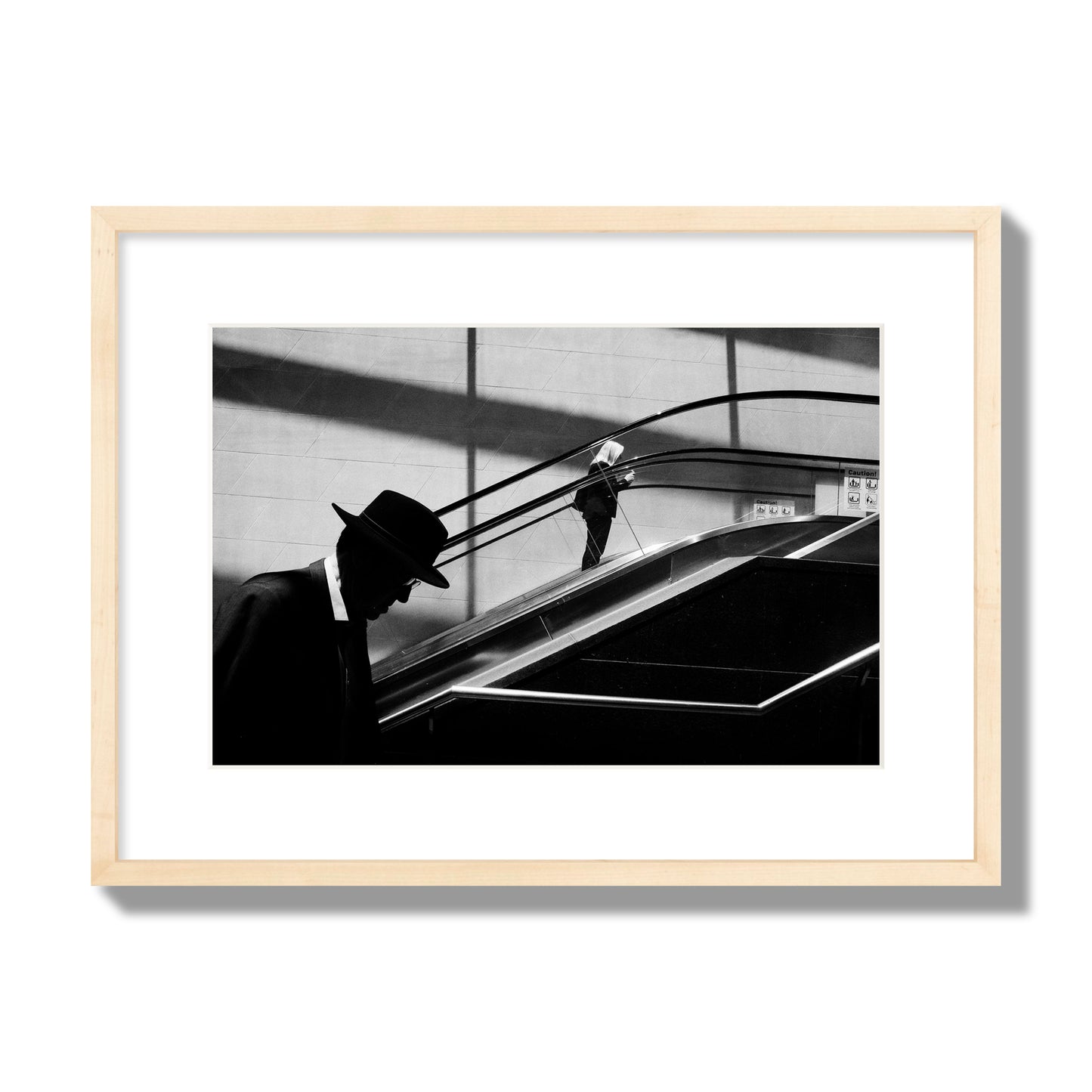 Fine art black and white street photograph of a man ascending an escalator. Archival pigment print, medium size, natural wood frame.