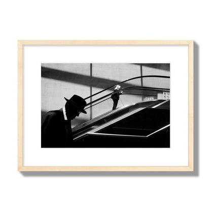 Fine art black and white street photograph of a man ascending an escalator. Archival pigment print, medium size, natural wood frame.