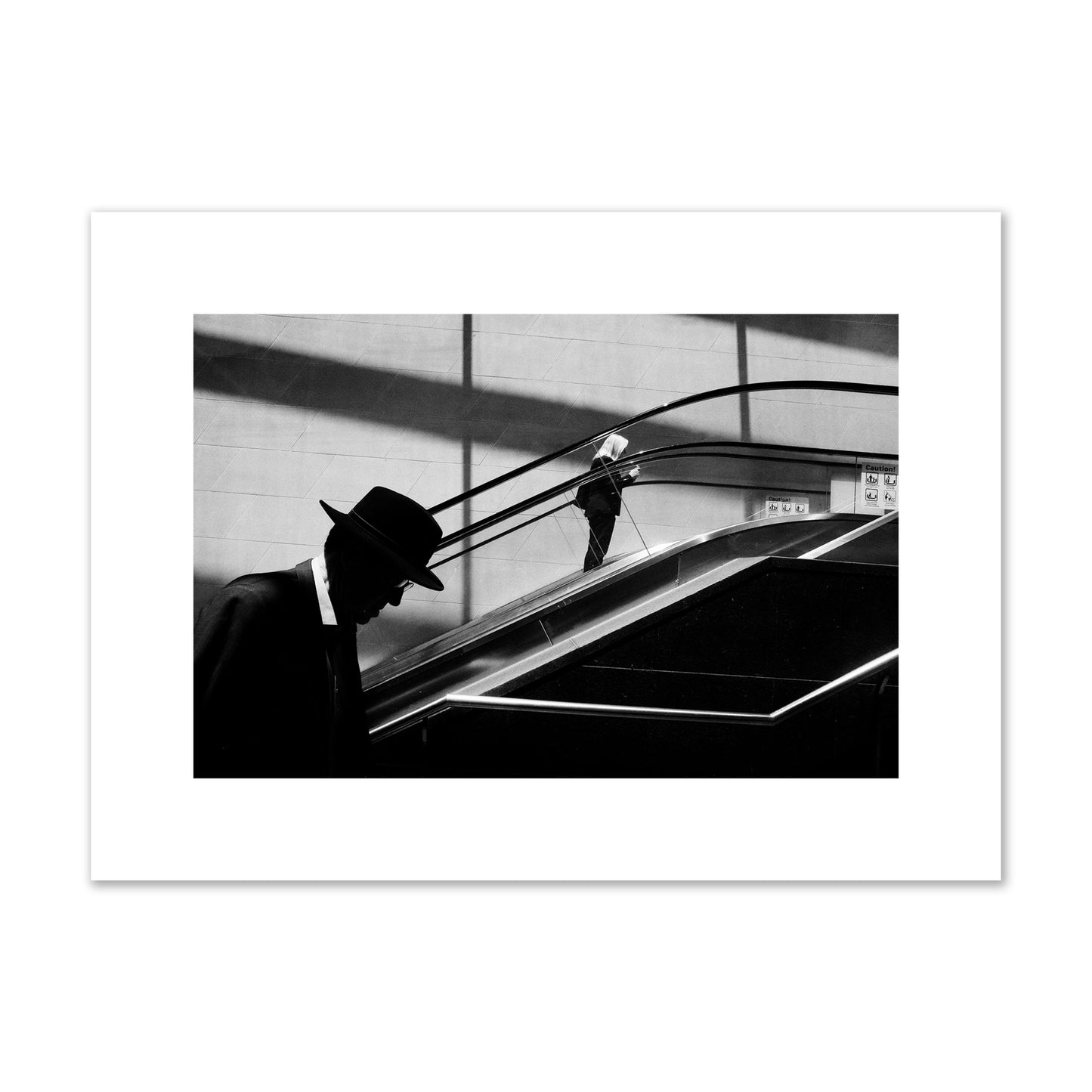 Fine art black and white street photograph of a man ascending an escalator. Archival pigment print, medium size, print.