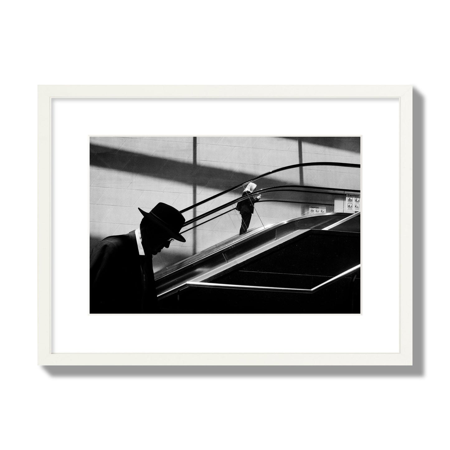 Fine art black and white street photograph of a man ascending an escalator. Archival pigment print, medium size, white frame.