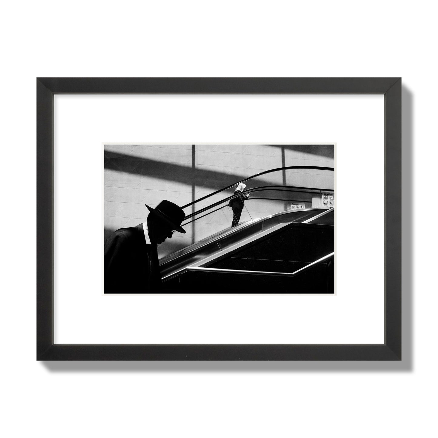 Fine art black and white street photograph of a man ascending an escalator. Archival pigment print, small size, black frame.