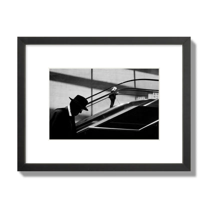 Fine art black and white street photograph of a man ascending an escalator. Archival pigment print, small size, black frame.