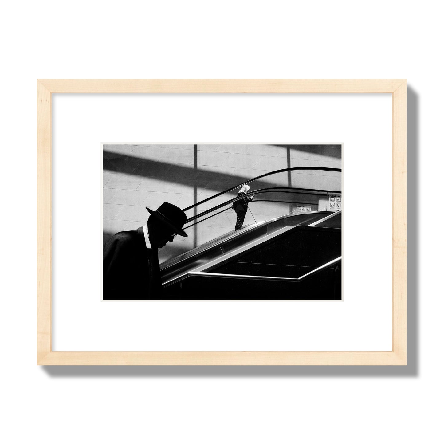 Fine art black and white street photograph of a man ascending an escalator. Archival pigment print, small size, natural wood frame.