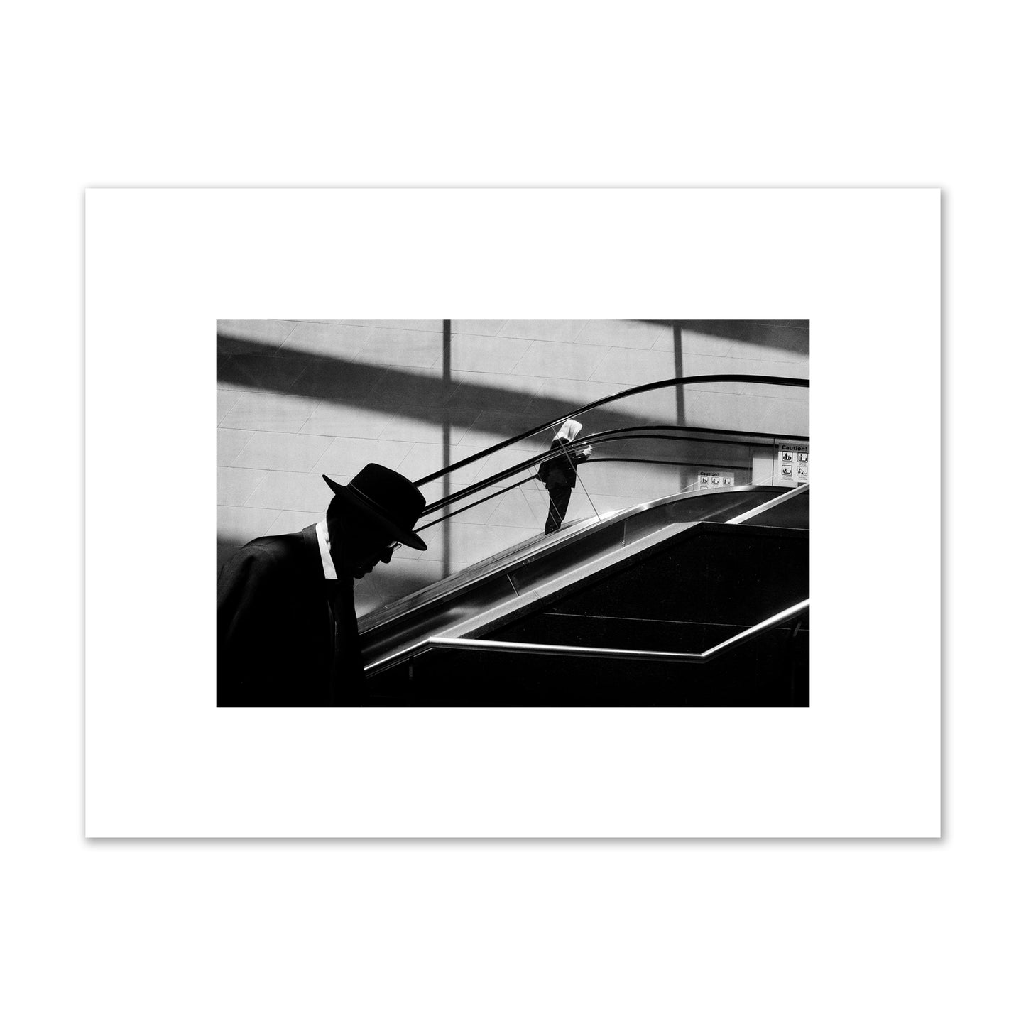 Fine art black and white street photograph of a man ascending an escalator. Archival pigment print, small size, print.