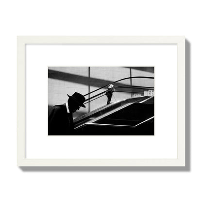 Fine art black and white street photograph of a man ascending an escalator. Archival pigment print, small size, white frame.