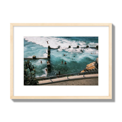 Fine art street photograph of a man jumping into the ocean. Archival pigment print, medium size, natural wood frame.