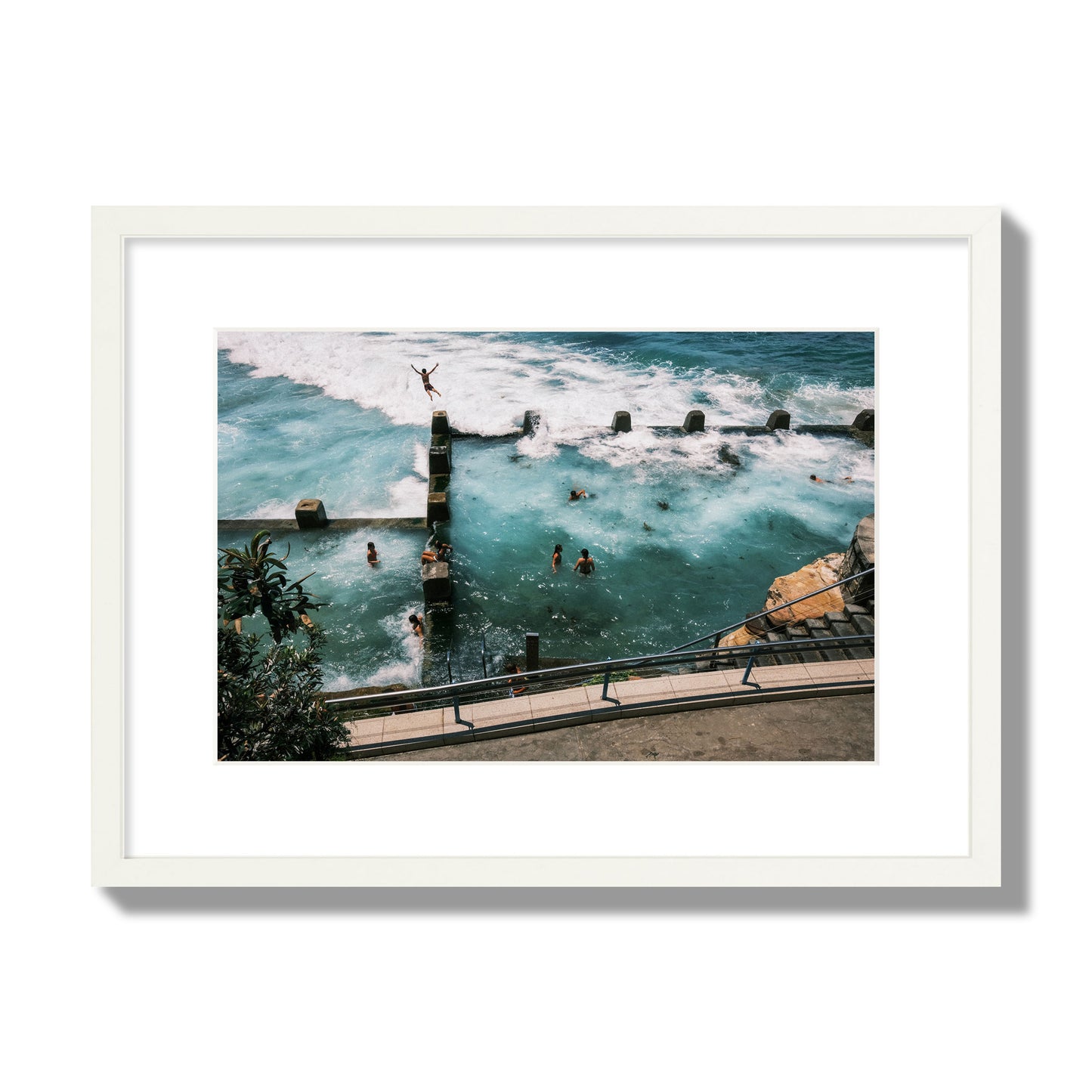 Fine art street photograph of a man jumping into the ocean. Archival pigment print, medium size, white frame.