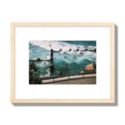 Fine art street photograph of a man jumping into the ocean. Archival pigment print, small size, natural wood frame.