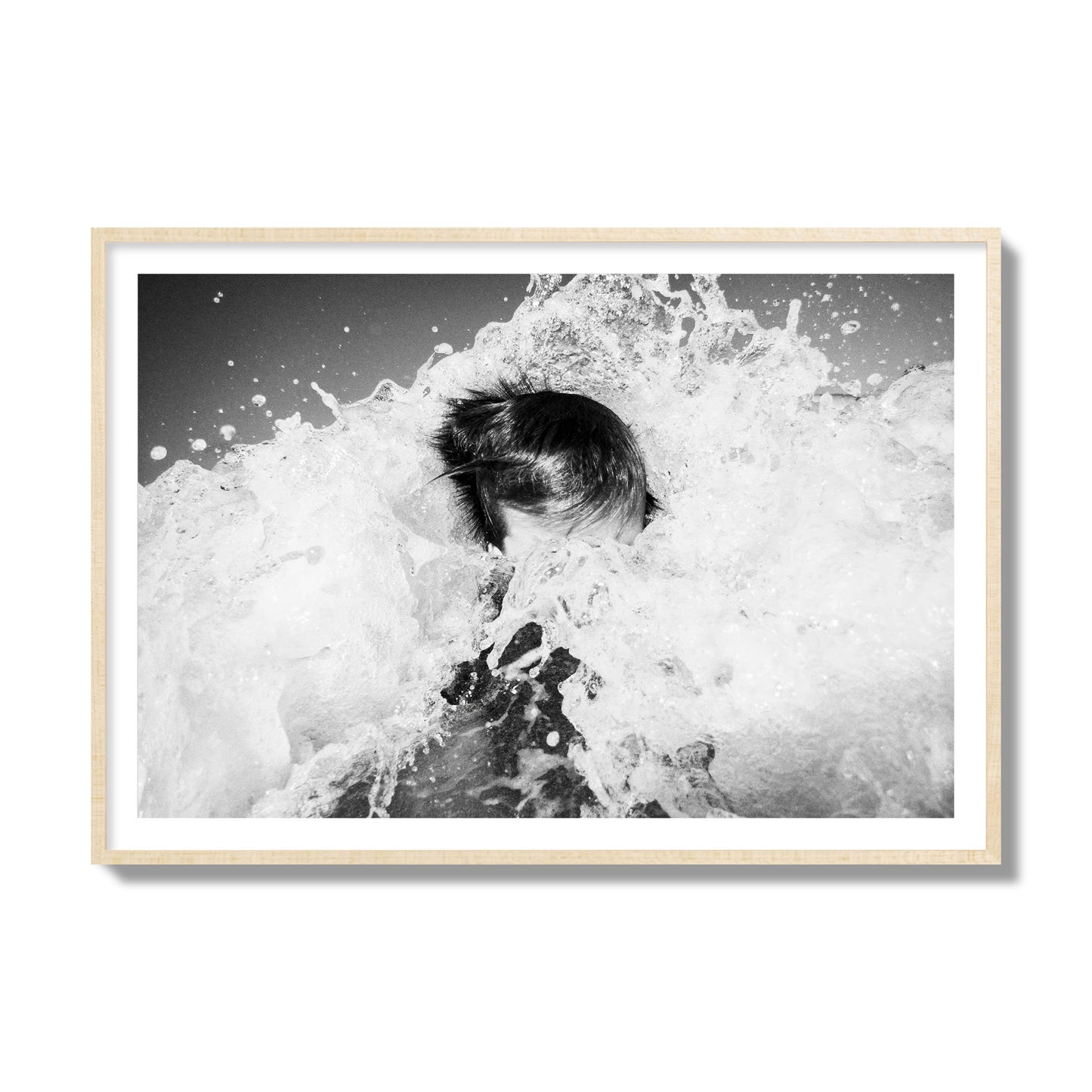 Fine art street photograph of an ocean wave crashing over a swimmer. Archival pigment print, collector size, natural wood frame.