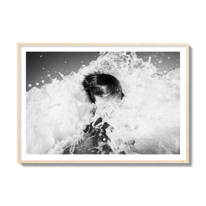 Fine art street photograph of an ocean wave crashing over a swimmer. Archival pigment print, collector size, natural wood frame.
