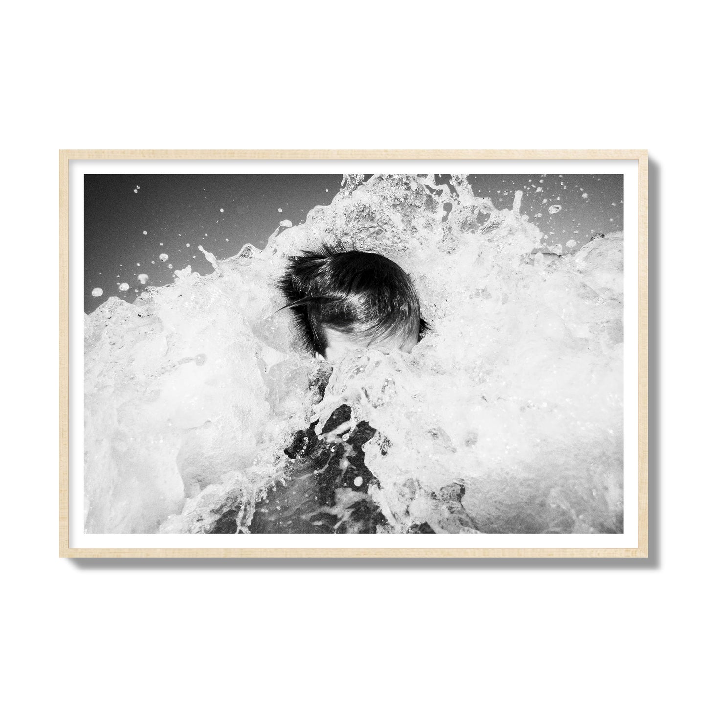 Fine art street photograph of an ocean wave crashing over a swimmer. Archival pigment print, gallery size, natural wood frame.