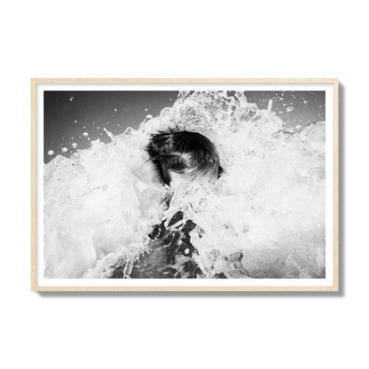 Fine art street photograph of an ocean wave crashing over a swimmer. Archival pigment print, gallery size, natural wood frame.