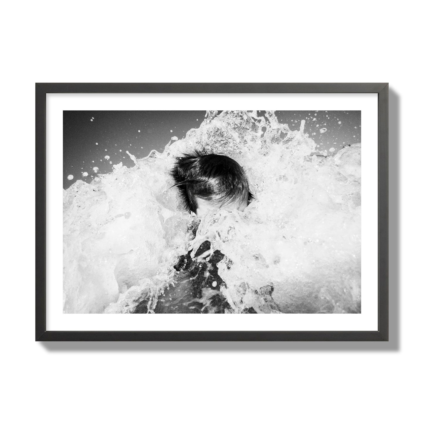 Fine art street photograph of an ocean wave crashing over a swimmer. Archival pigment print, giant size, black frame.