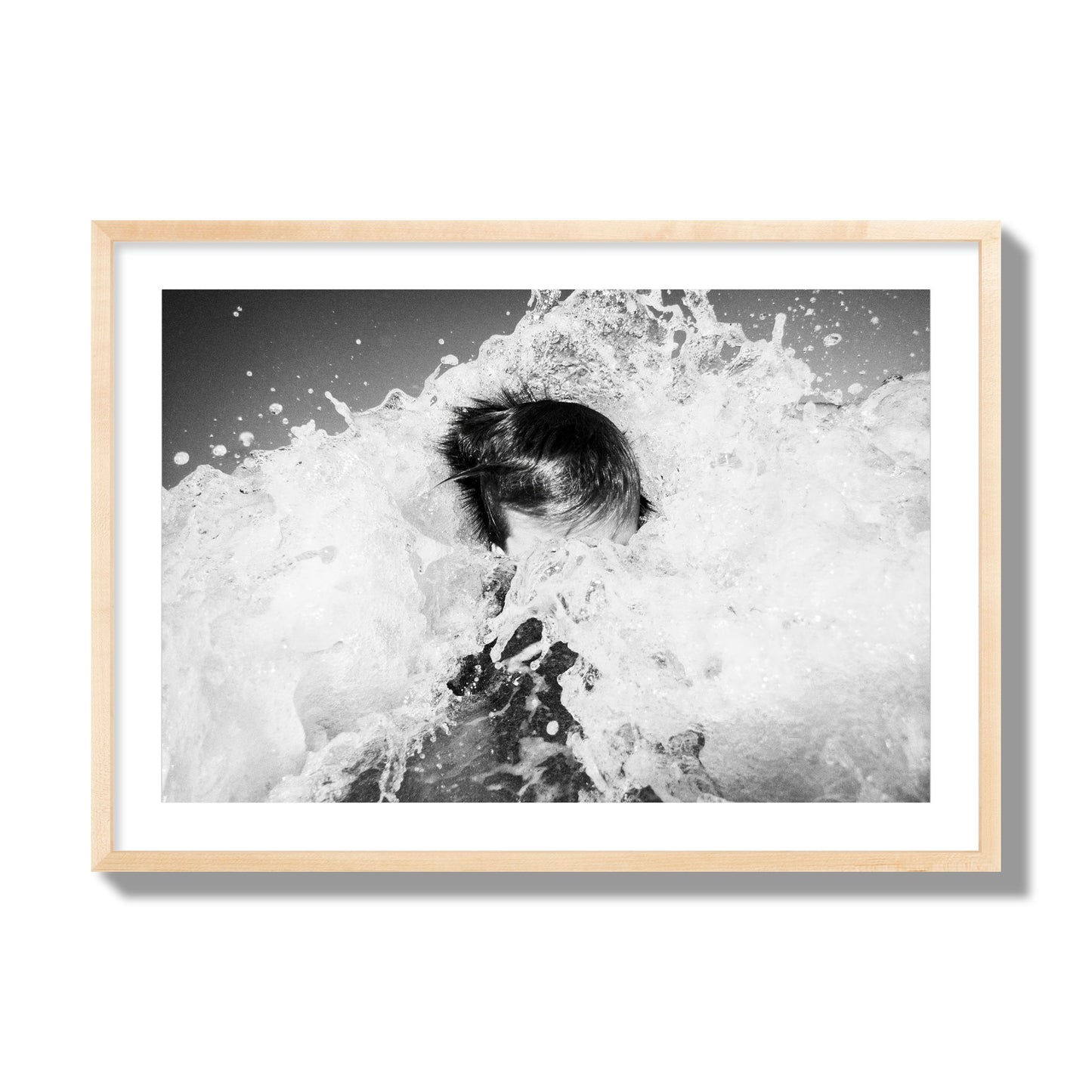 Fine art street photograph of an ocean wave crashing over a swimmer. Archival pigment print, giant size, natural wood frame.
