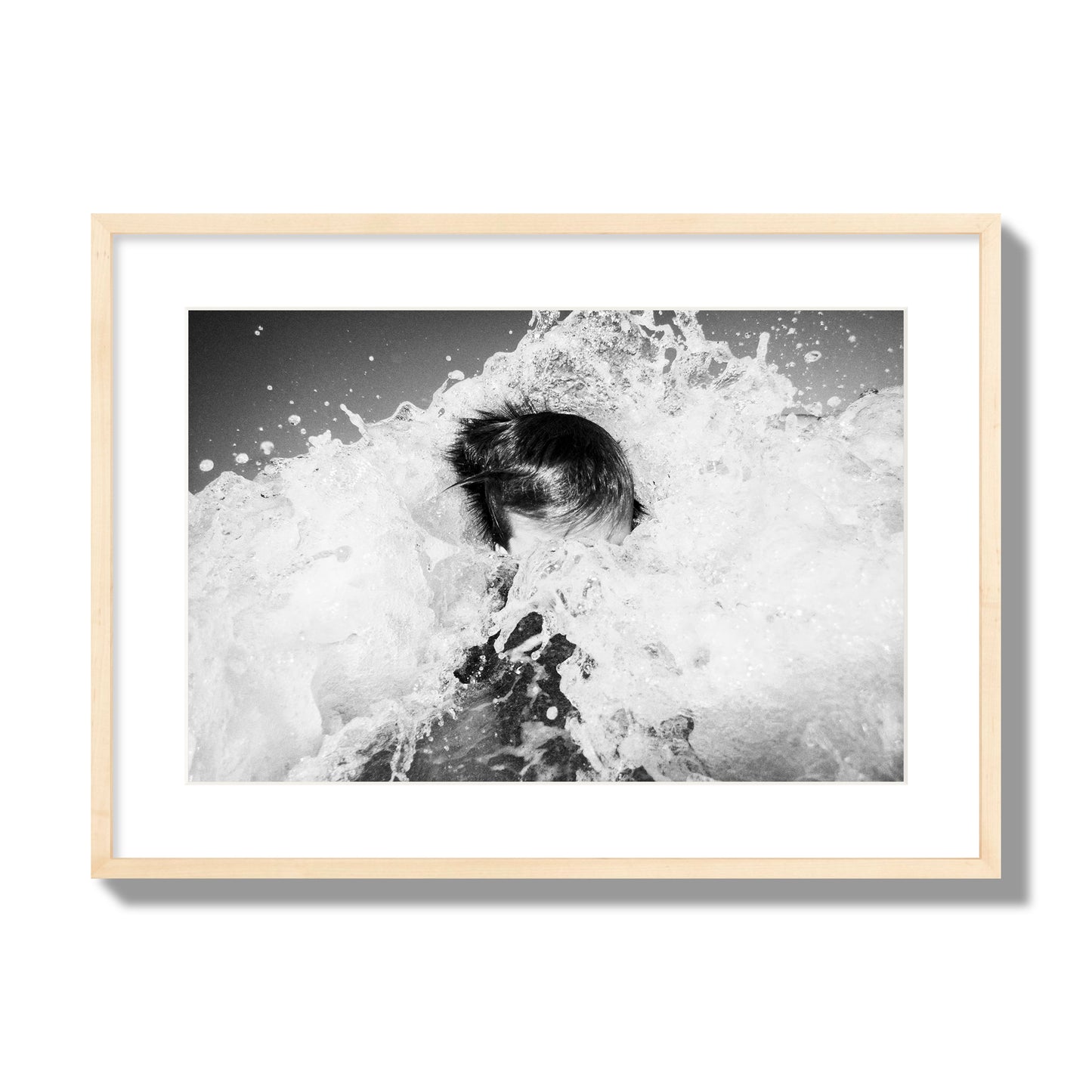 Fine art street photograph of an ocean wave crashing over a swimmer. Archival pigment print, large size, natural wood frame.