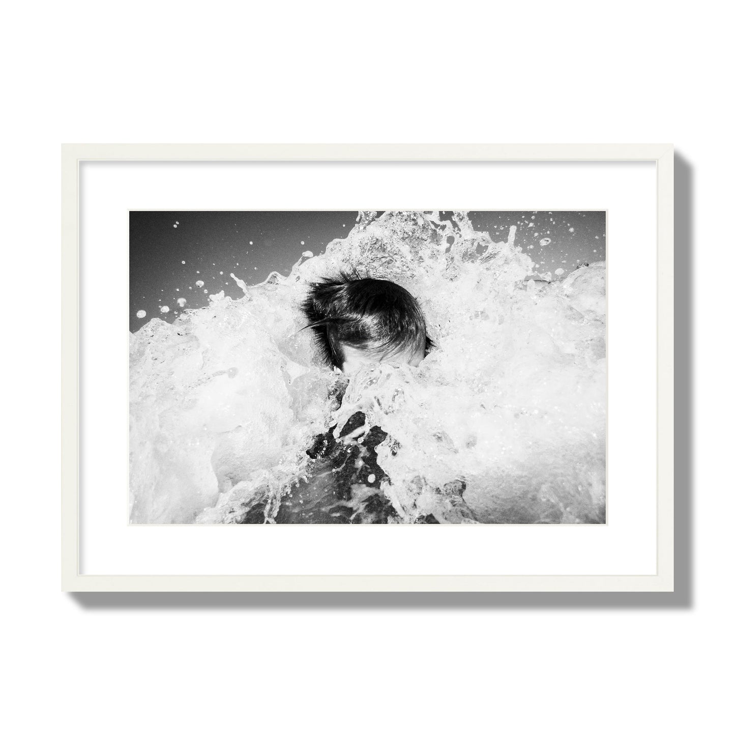 Fine art street photograph of an ocean wave crashing over a swimmer. Archival pigment print, large size, white frame.