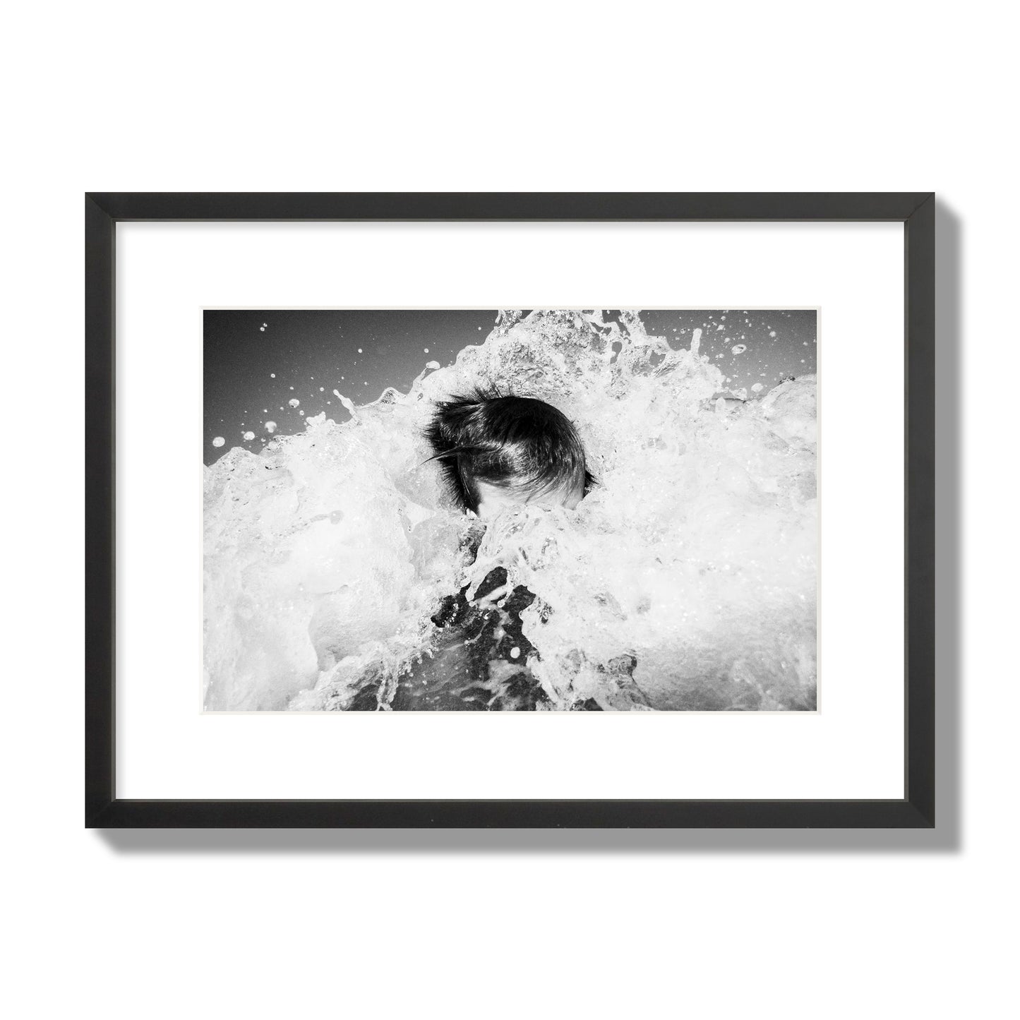 Fine art street photograph of an ocean wave crashing over a swimmer. Archival pigment print, medium size, black frame.