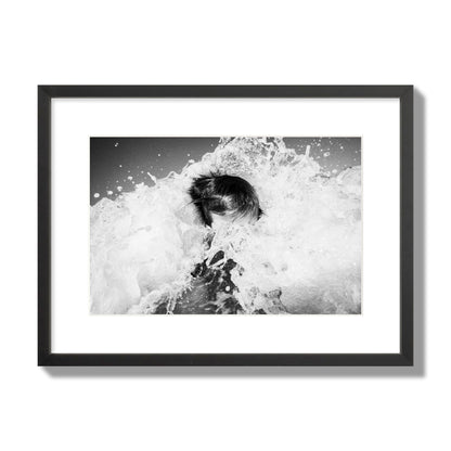 Fine art street photograph of an ocean wave crashing over a swimmer. Archival pigment print, medium size, black frame.