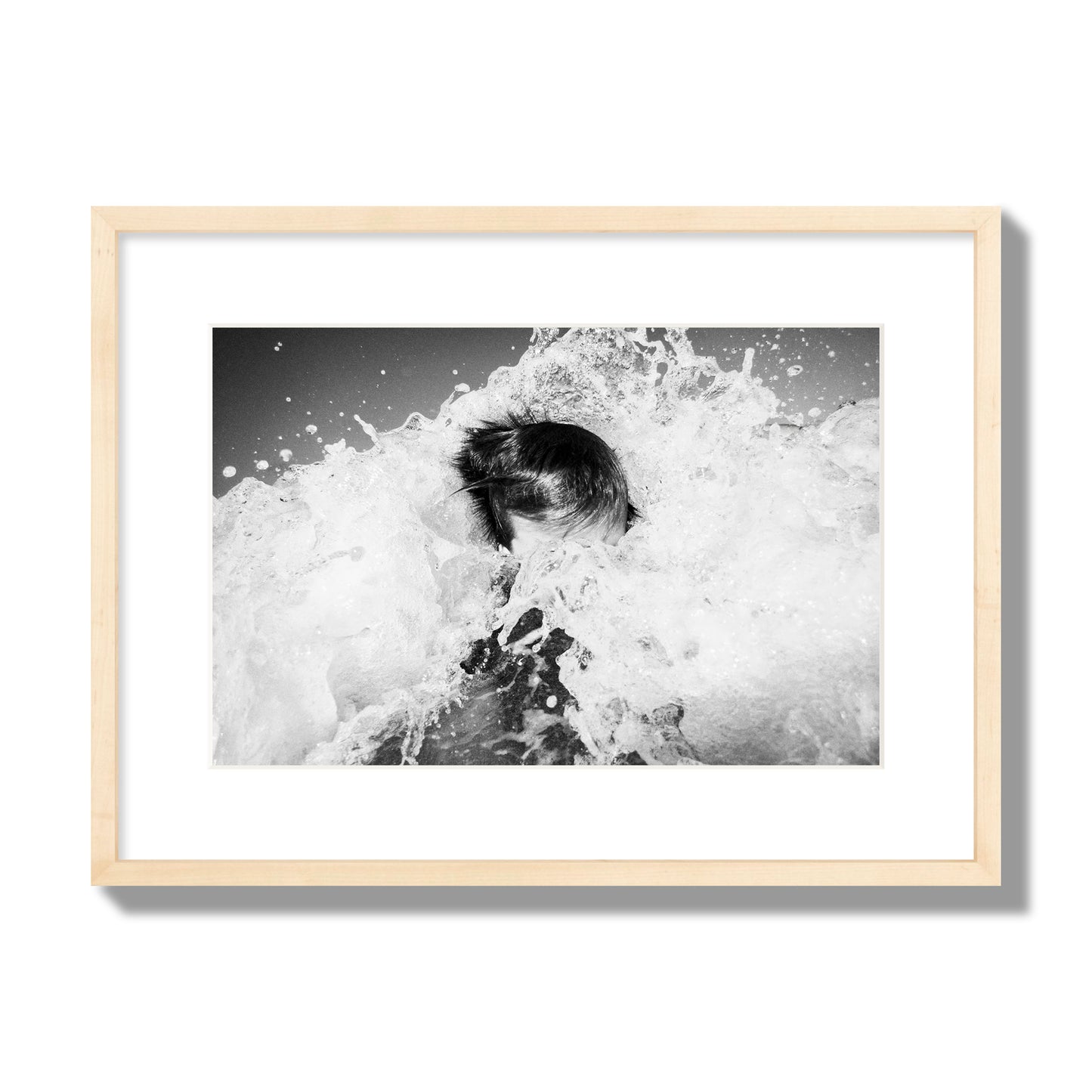 Fine art street photograph of an ocean wave crashing over a swimmer. Archival pigment print, medium size, natural wood frame.