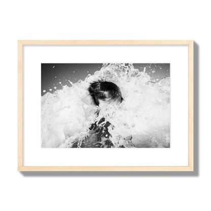 Fine art street photograph of an ocean wave crashing over a swimmer. Archival pigment print, medium size, natural wood frame.