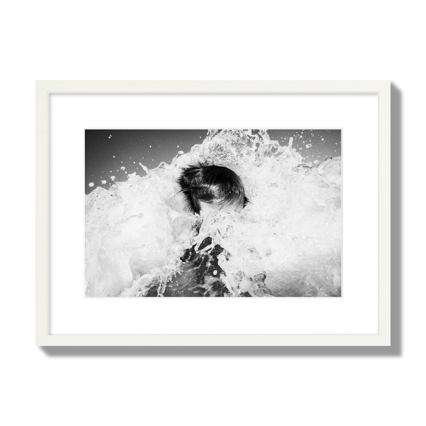 Fine art street photograph of an ocean wave crashing over a swimmer. Archival pigment print, medium size, white frame.