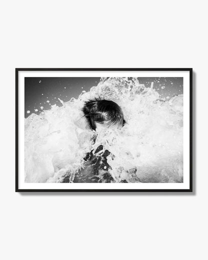 Fine art street photograph of an ocean wave crashing over a swimmer. Archival pigment print, black frame.