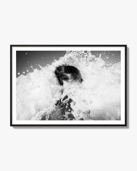 Fine art street photograph of an ocean wave crashing over a swimmer. Archival pigment print, black frame.