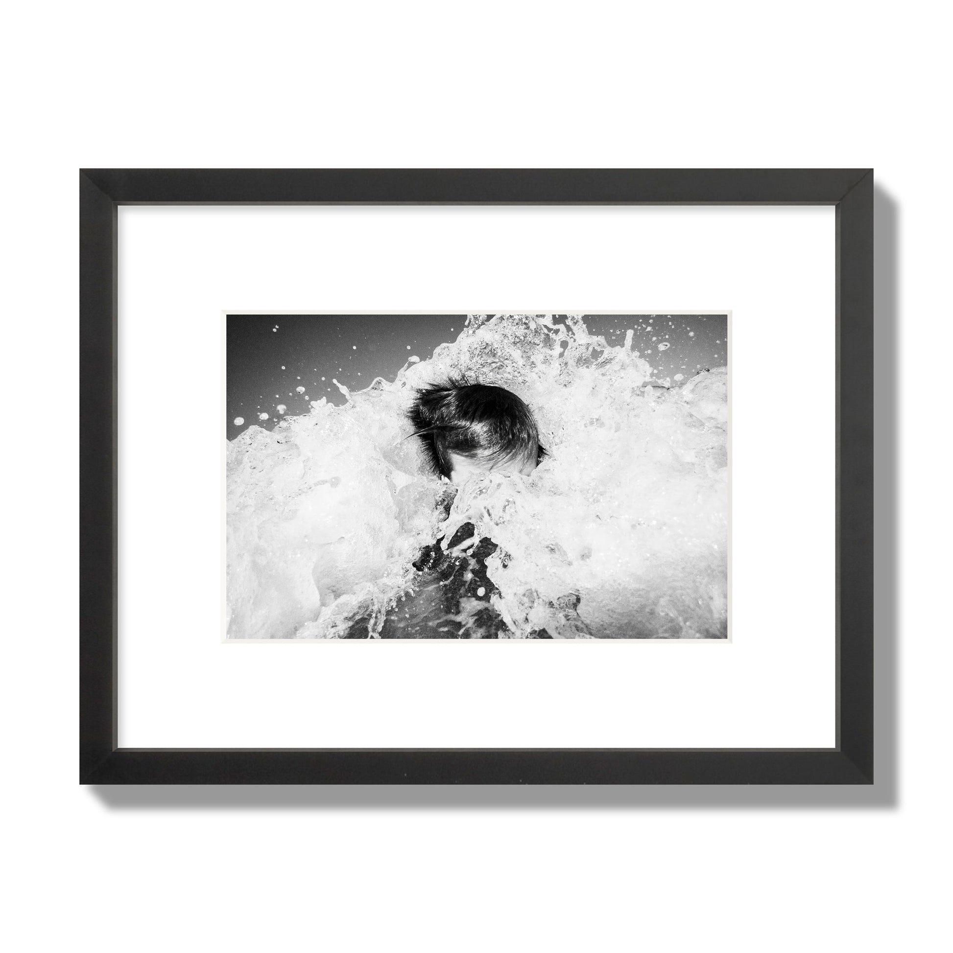 Fine art street photograph of an ocean wave crashing over a swimmer. Archival pigment print, small size, black frame.