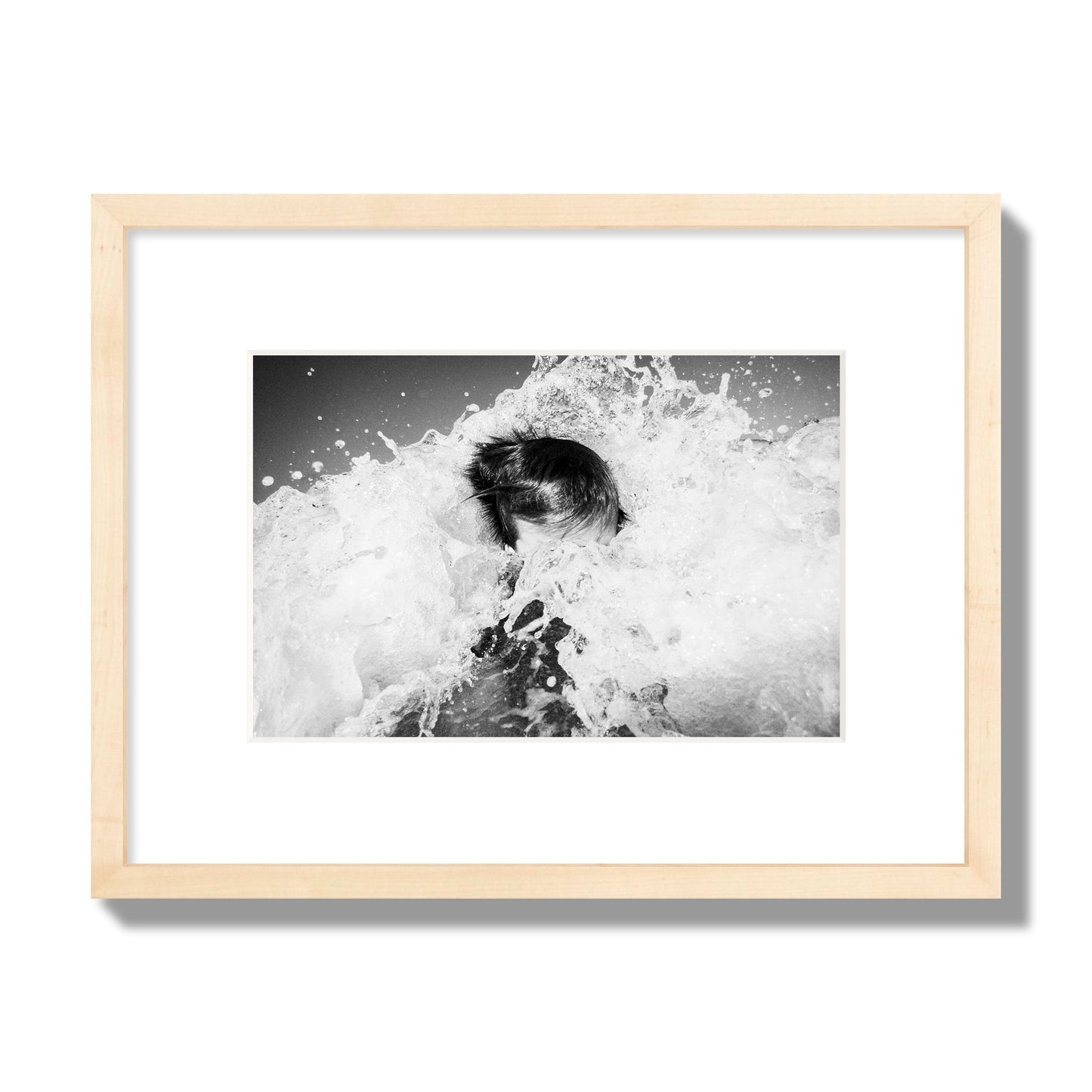 Fine art street photograph of an ocean wave crashing over a swimmer. Archival pigment print, small size, natural wood frame.