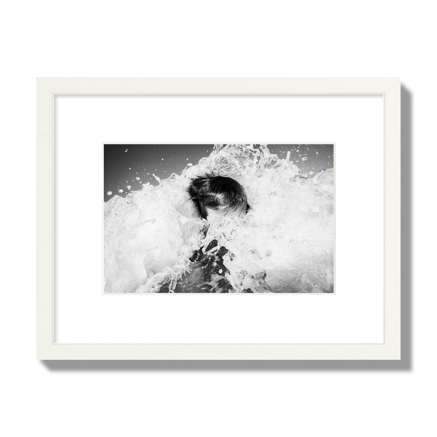 Fine art street photograph of an ocean wave crashing over a swimmer. Archival pigment print, small size, white frame.