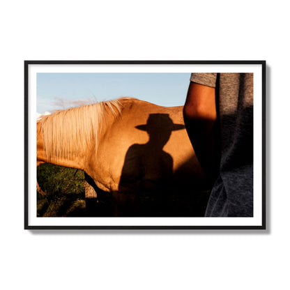 Fine art photo of a cowboy's shadow cast against the side of a horse at sunset. Archival pigment print, collector size, black frame.