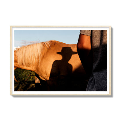 Fine art photo of a cowboy's shadow cast against the side of a horse at sunset. Archival pigment print, gallery size, natural wood frame.
