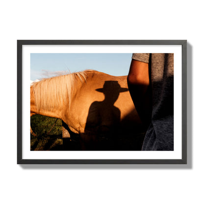 Fine art photo of a cowboy's shadow cast against the side of a horse at sunset. Archival pigment print, giant size, black frame.