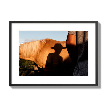 Fine art photo of a cowboy's shadow cast against the side of a horse at sunset. Archival pigment print, large size, black frame.
