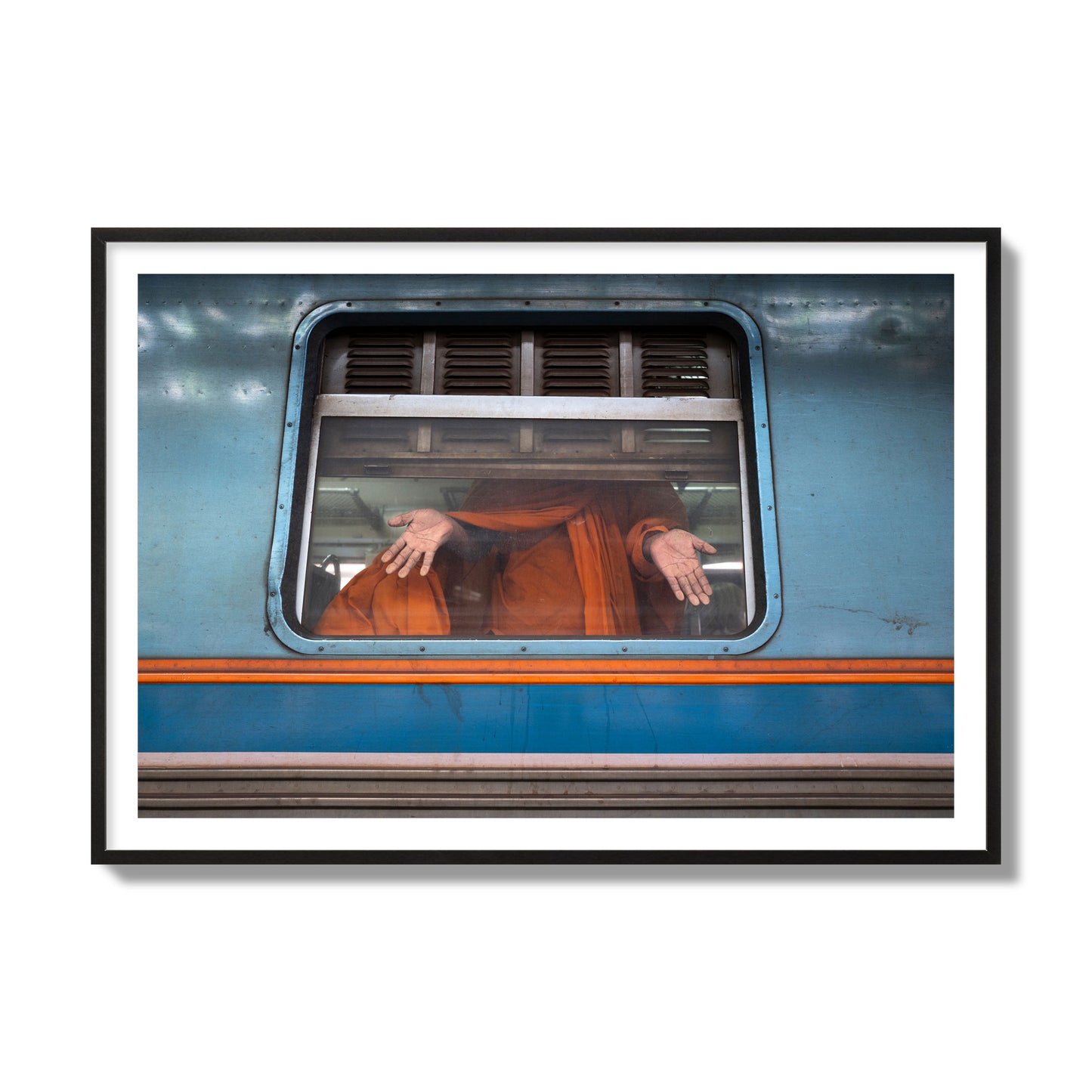 Fine art photograph of a Buddhist monk standing with open hands at a train car window. Archival pigment print, collector size, black frame.