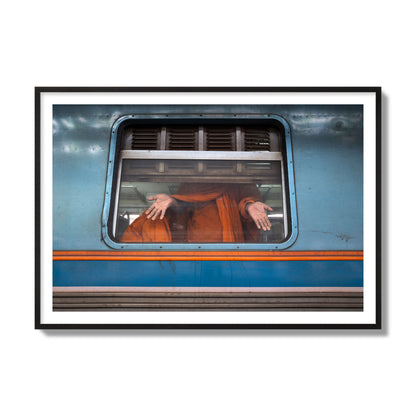 Fine art photograph of a Buddhist monk standing with open hands at a train car window. Archival pigment print, collector size, black frame.