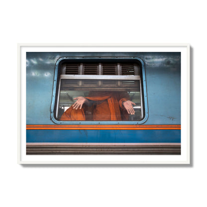 Fine art photograph of a Buddhist monk standing with open hands at a train car window. Archival pigment print, collector size, white frame.