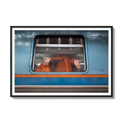 Fine art photograph of a Buddhist monk standing with open hands at a train car window. Archival pigment print, gallery size, black frame.