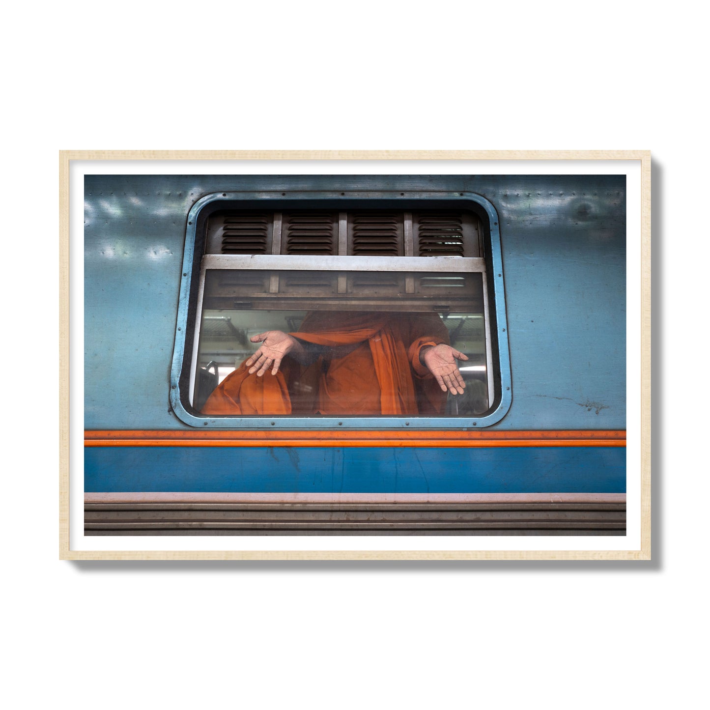 Fine art photograph of a Buddhist monk standing with open hands at a train car window. Archival pigment print, gallery size, natural wood frame.