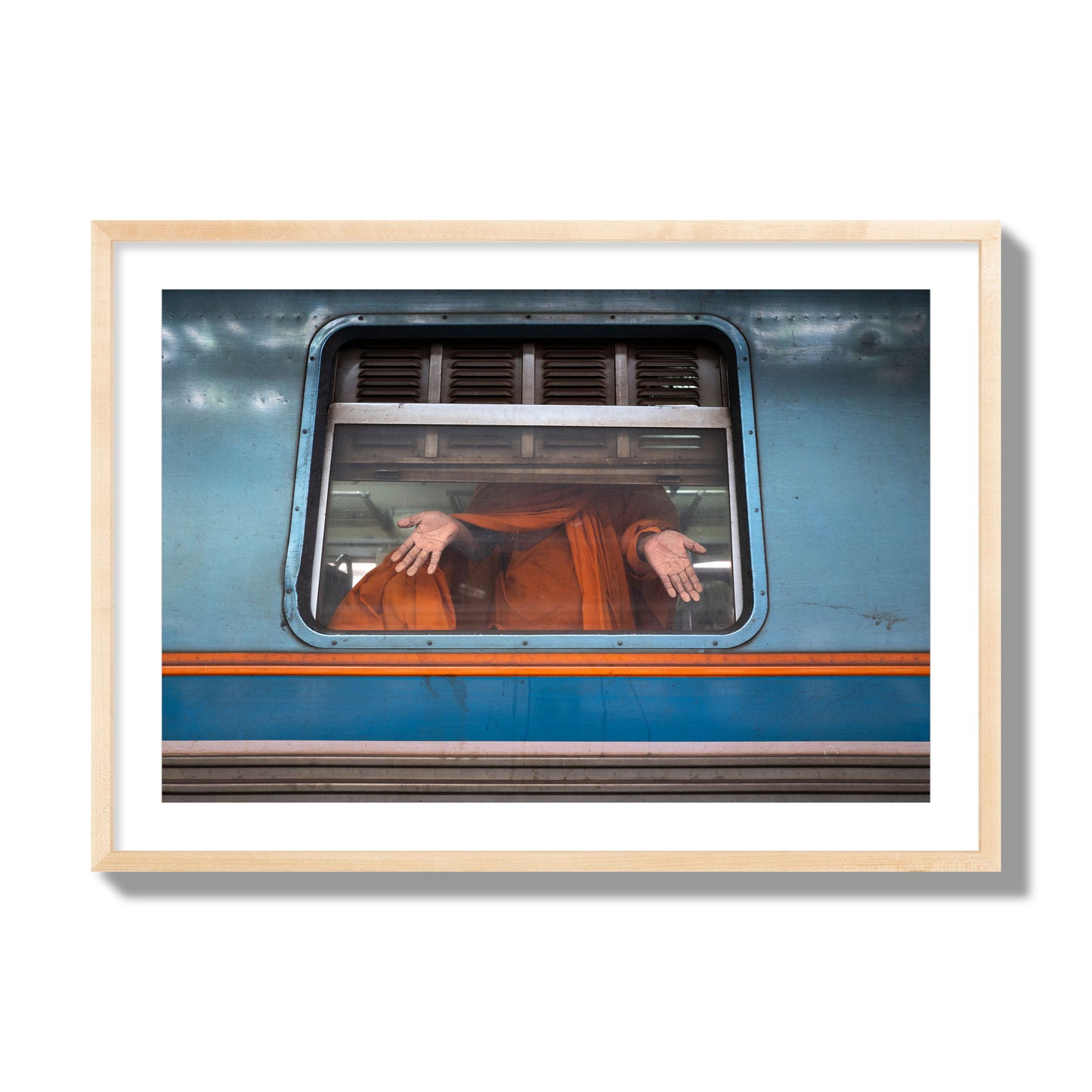 Fine art photograph of a Buddhist monk standing with open hands at a train car window. Archival pigment print, giant size, natural wood frame.
