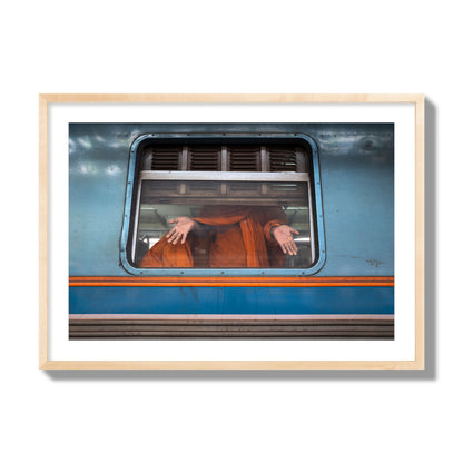 Fine art photograph of a Buddhist monk standing with open hands at a train car window. Archival pigment print, giant size, natural wood frame.