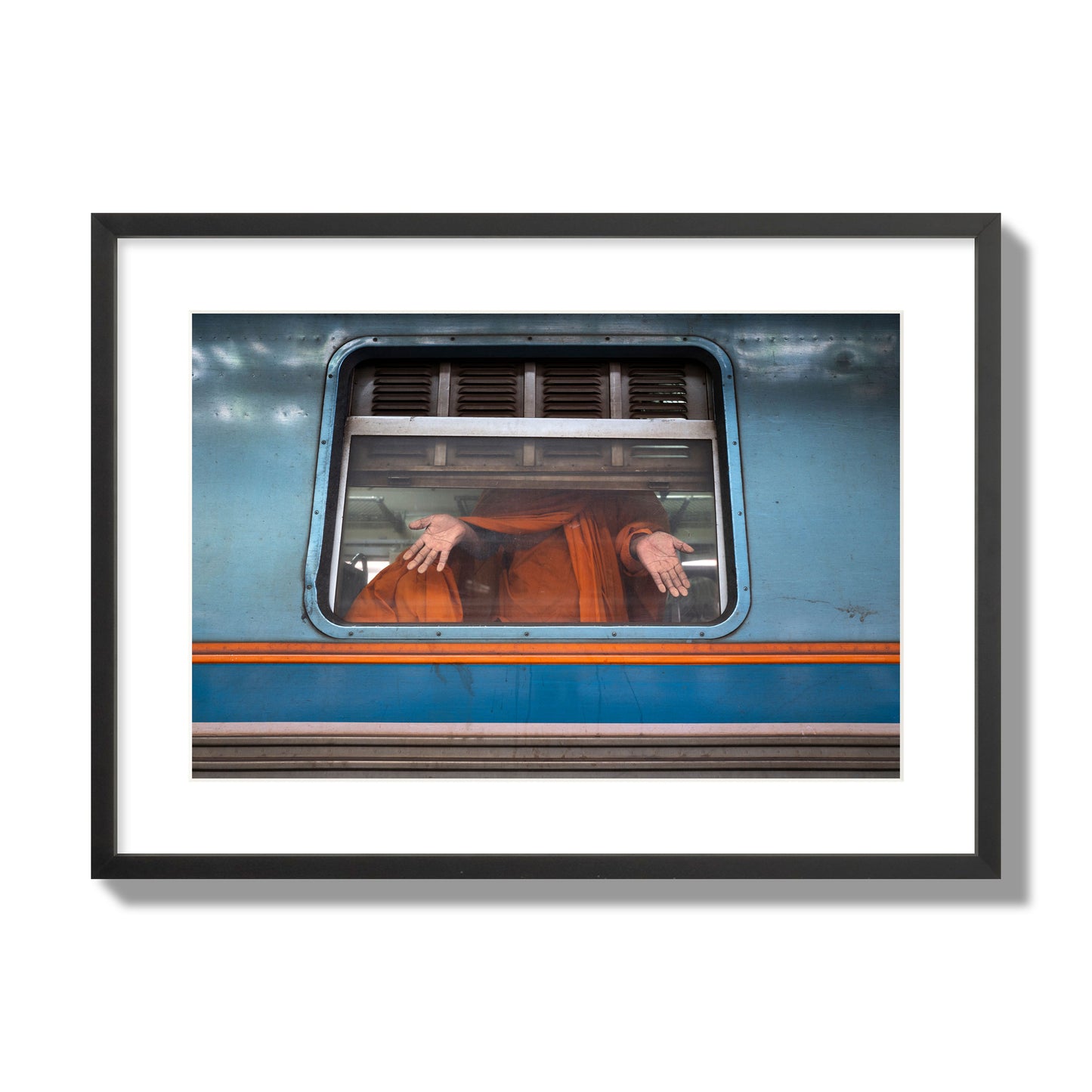 Fine art photograph of a Buddhist monk standing with open hands at a train car window. Archival pigment print, large size, black frame.