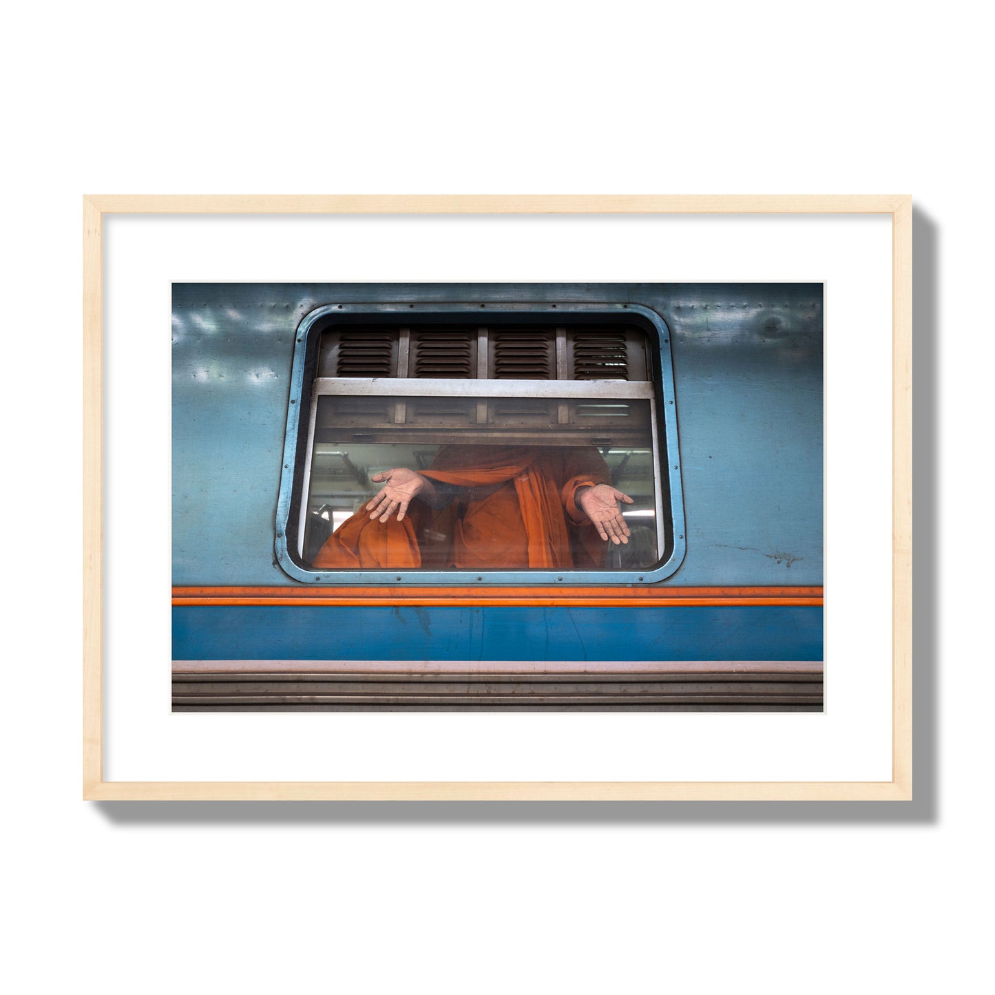 Fine art photograph of a Buddhist monk standing with open hands at a train car window. Archival pigment print, large size, natural wood frame.