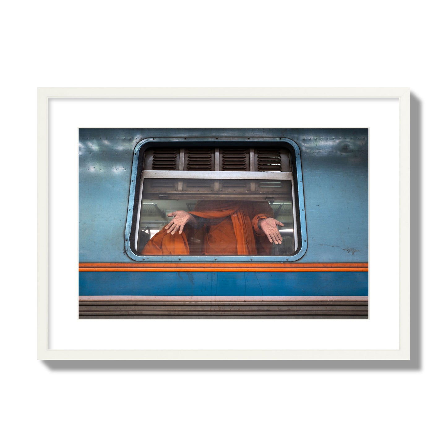 Fine art photograph of a Buddhist monk standing with open hands at a train car window. Archival pigment print, large size, white frame.