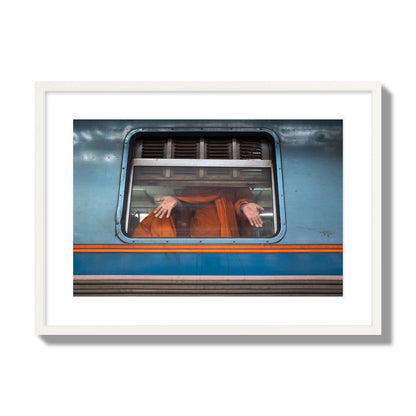 Fine art photograph of a Buddhist monk standing with open hands at a train car window. Archival pigment print, large size, white frame.