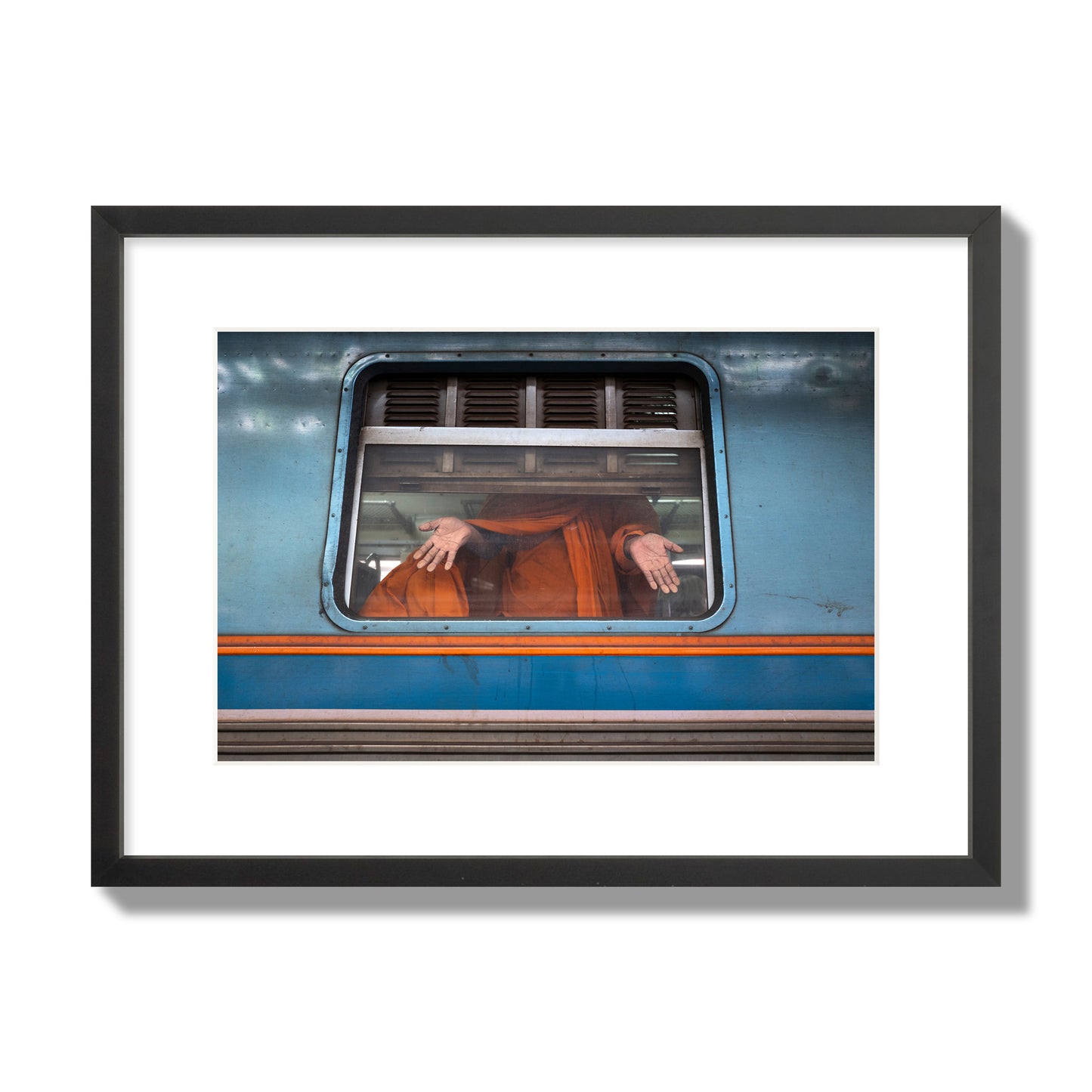 Fine art photograph of a Buddhist monk standing with open hands at a train car window. Archival pigment print, medium size, black frame.