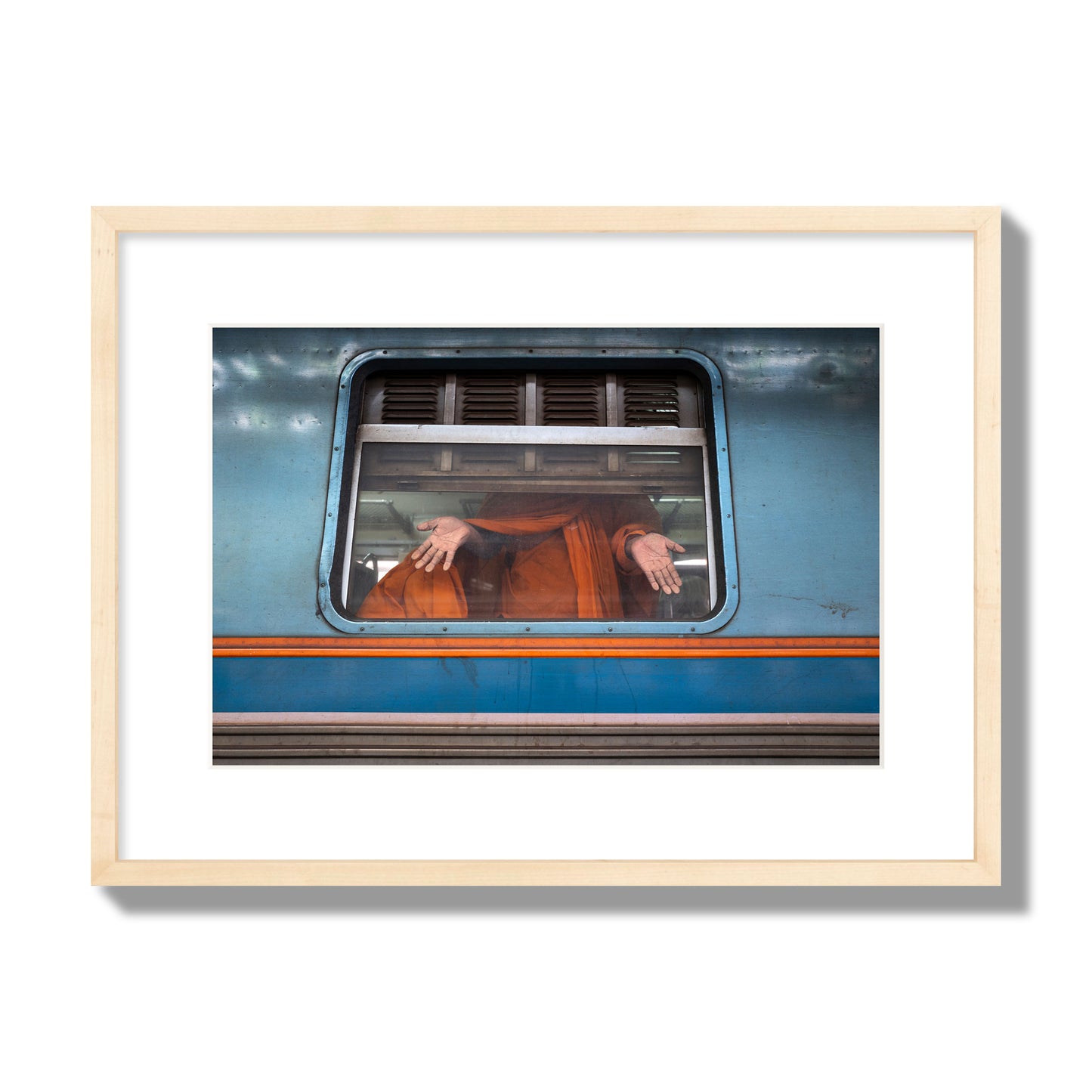Fine art photograph of a Buddhist monk standing with open hands at a train car window. Archival pigment print, medium size, natural wood frame.